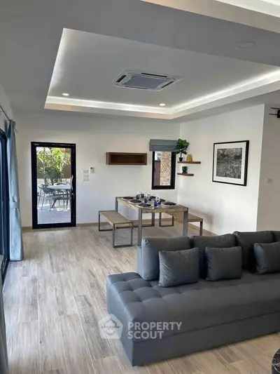 Modern living room with stylish furniture and open dining area, featuring elegant ceiling design and natural light.
