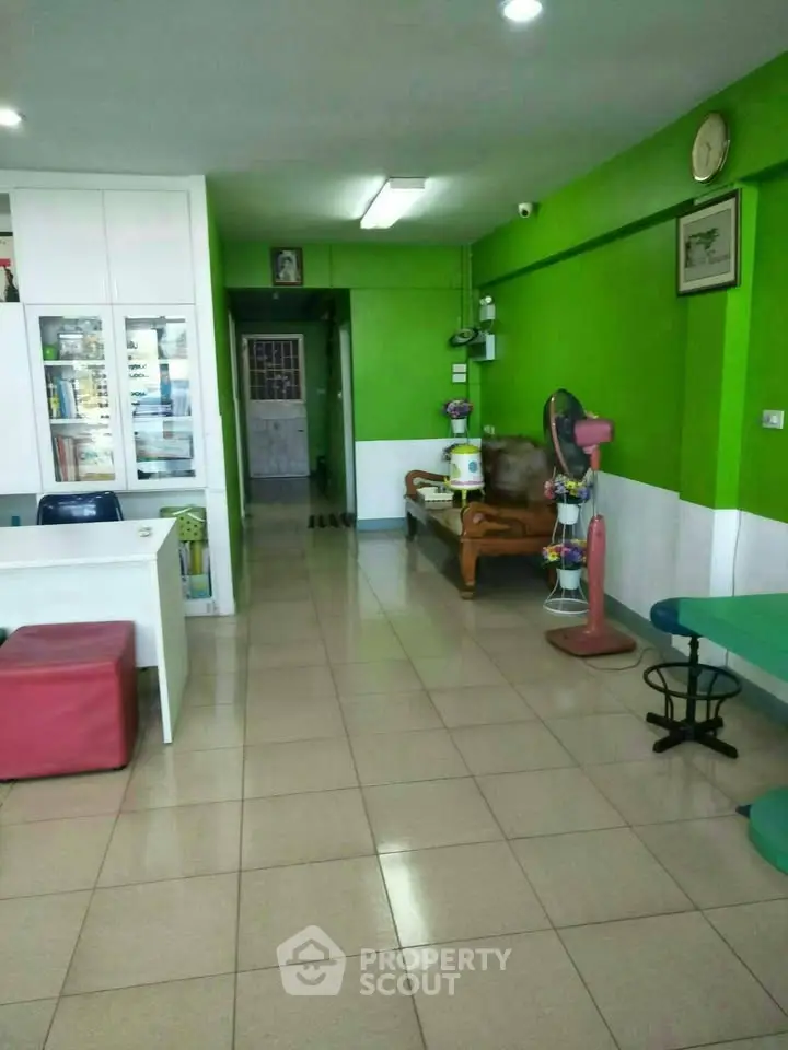 Spacious living area with vibrant green walls and tiled flooring, featuring cozy seating and modern decor.