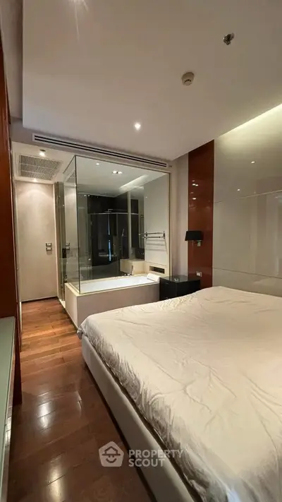 Luxurious bedroom with modern ensuite glass-walled bathtub, elegant wooden flooring, and ambient lighting.