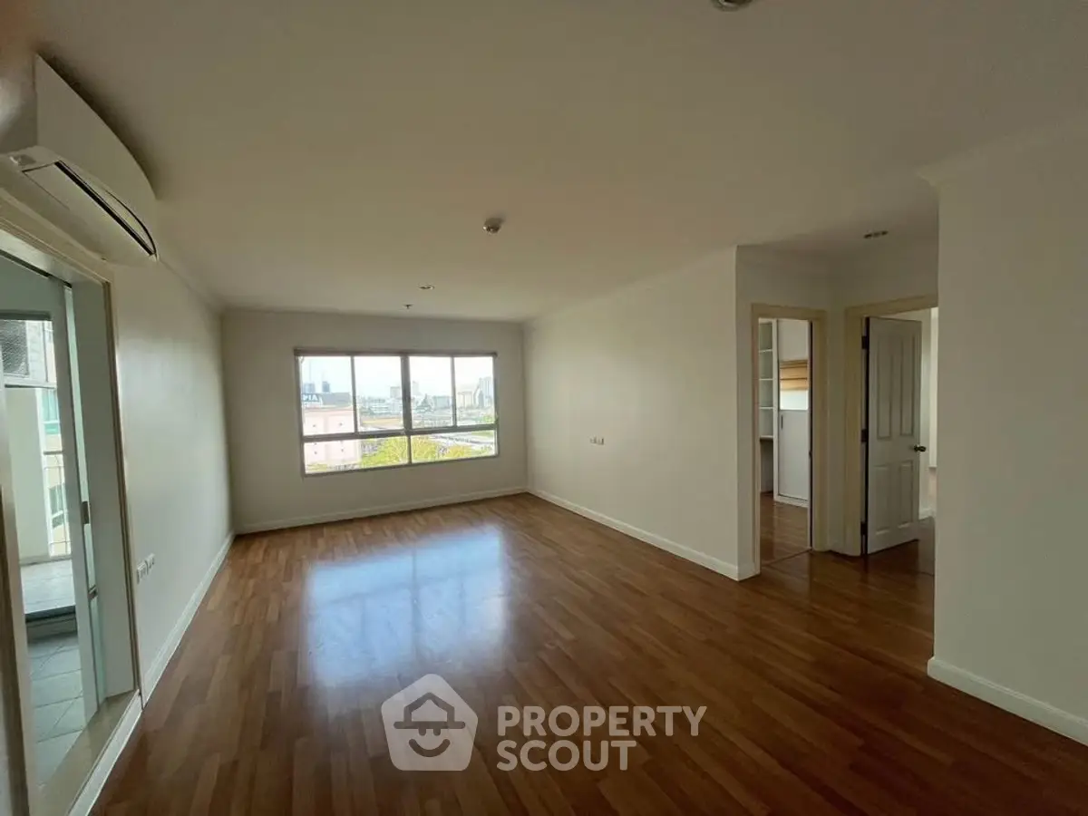 Spacious empty living room with wooden flooring and large window view.