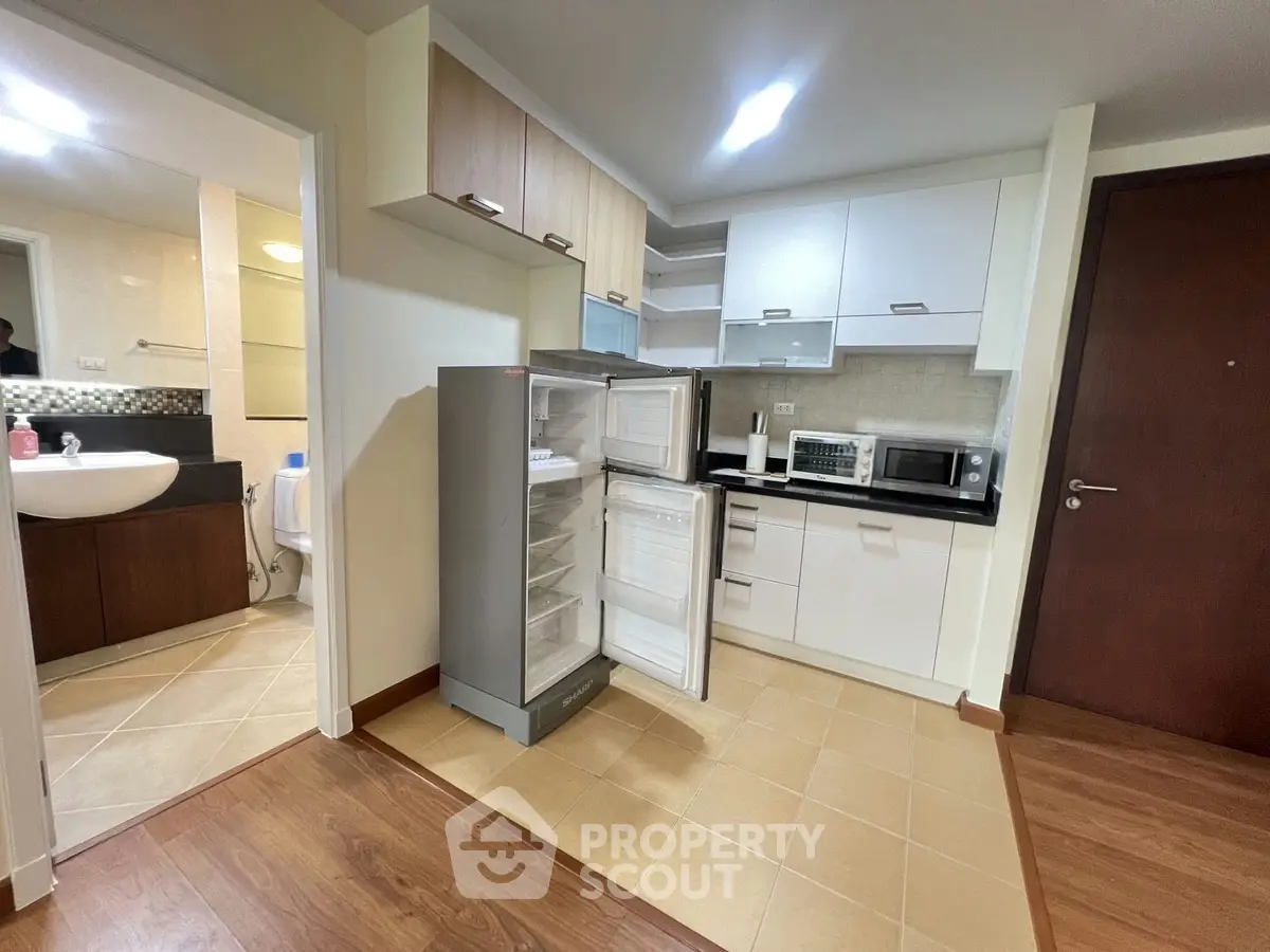 Modern kitchen with open fridge, adjacent to a bathroom, featuring sleek cabinetry and appliances.
