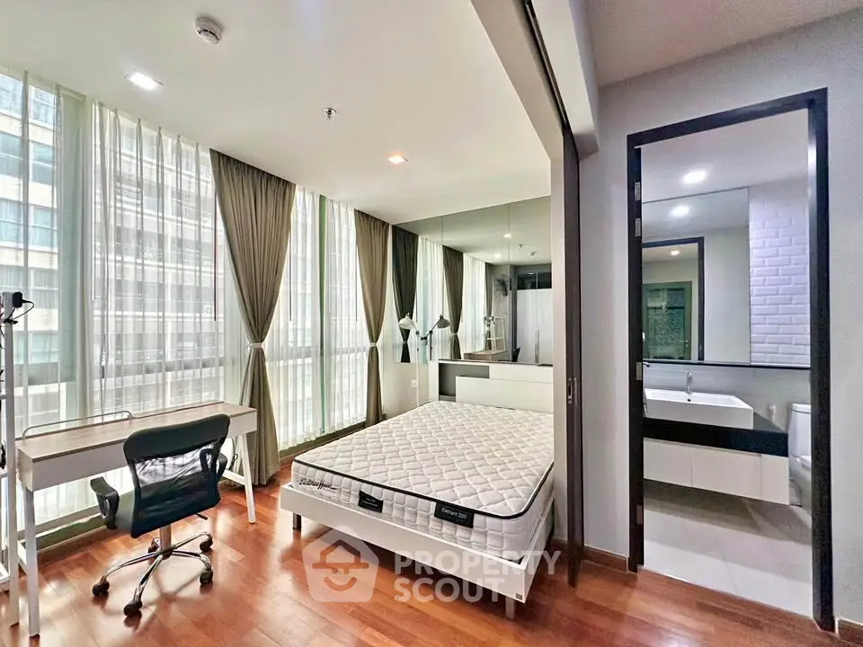 Modern bedroom with large windows, study desk, and ensuite bathroom in a high-rise apartment.