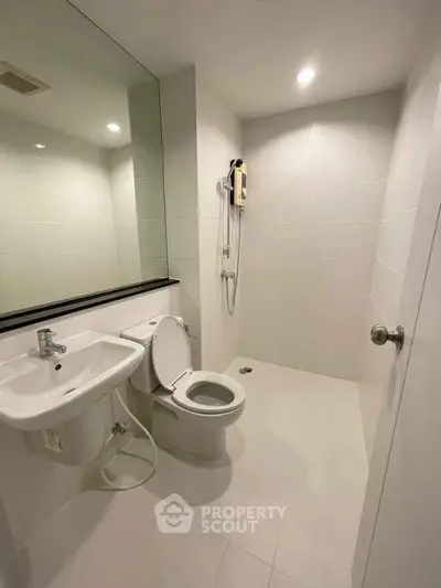 Modern minimalist bathroom with sleek fixtures and large mirror in a bright, white-tiled space.