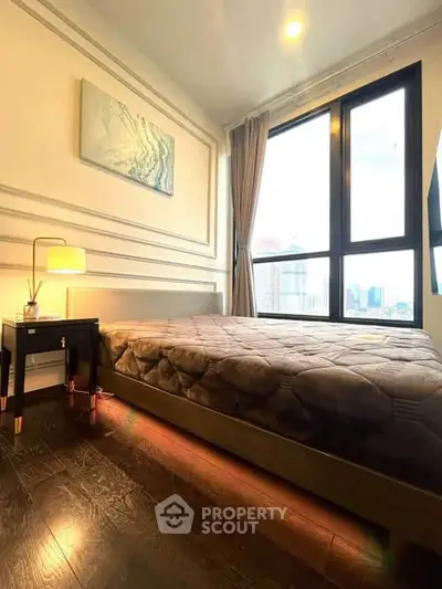 Modern bedroom with large window offering city view, elegant decor, and cozy lighting.