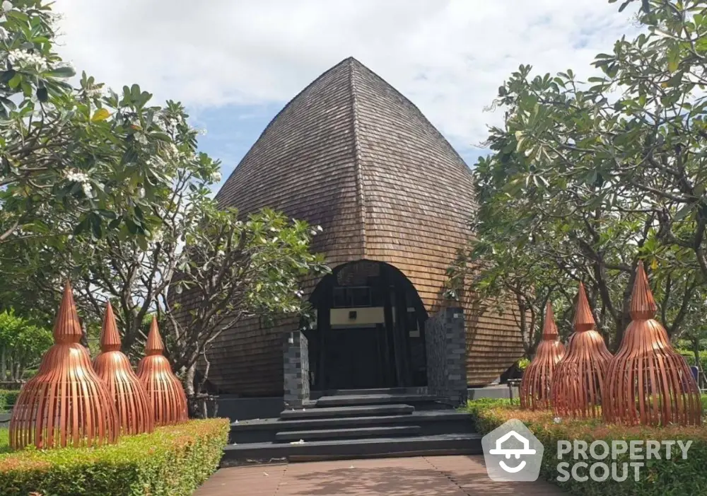 Unique architectural building with wooden facade surrounded by lush greenery and artistic sculptures.