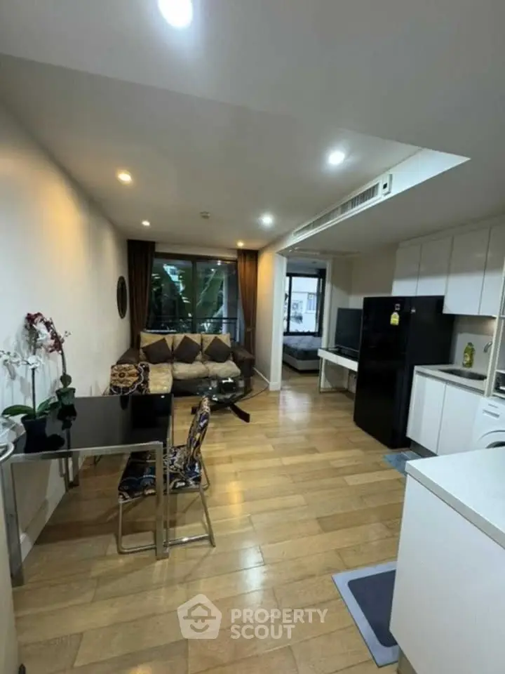Modern open-plan living room with kitchen, featuring sleek furniture and hardwood floors.