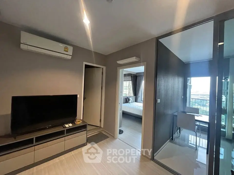 Modern living room with TV, air conditioning, and view into bedroom and balcony.