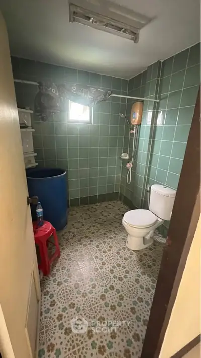 Cozy bathroom with green tiled walls and patterned floor, featuring a toilet and shower area.