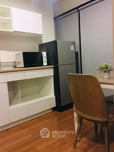 Modern kitchen with sleek appliances and wooden flooring, featuring a fridge and microwave for convenience.