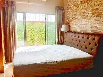 Cozy bedroom with large window and stylish brick accent wall, offering natural light and garden view.
