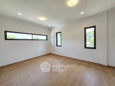 Spacious empty room with wooden flooring and large windows offering natural light.