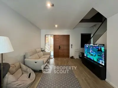Modern living room with cozy seating and large TV, featuring wooden flooring and stylish decor.