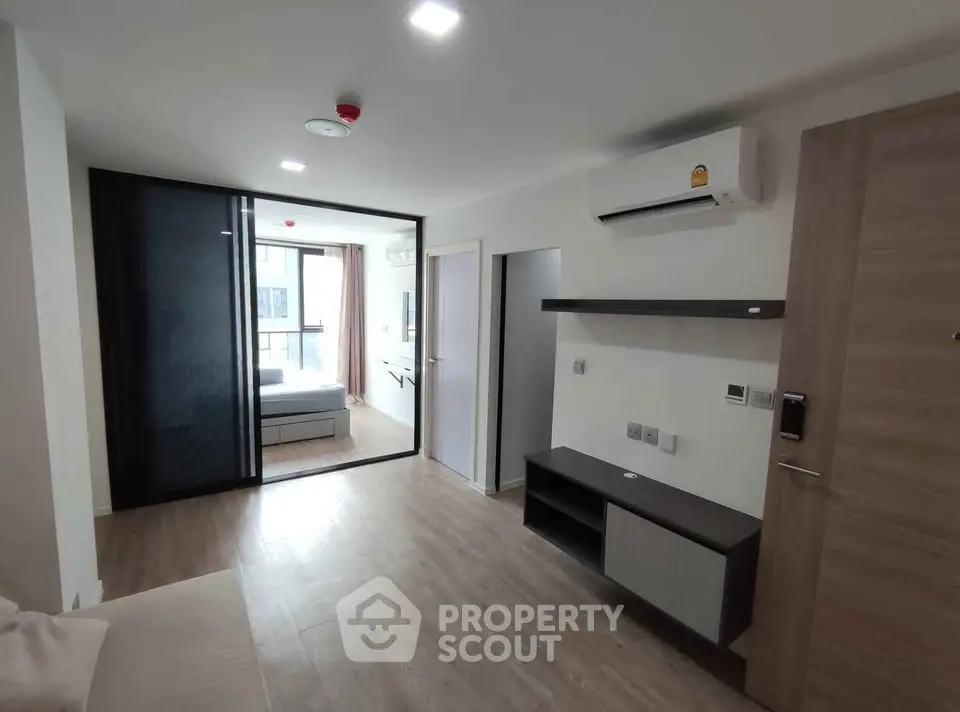 Modern apartment interior with wooden flooring and air conditioning, featuring a cozy living area and a glimpse of the bedroom.