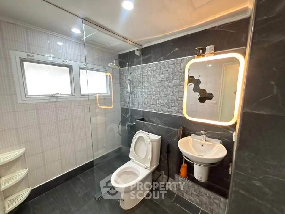Modern bathroom with sleek design, featuring glass shower and illuminated mirror.
