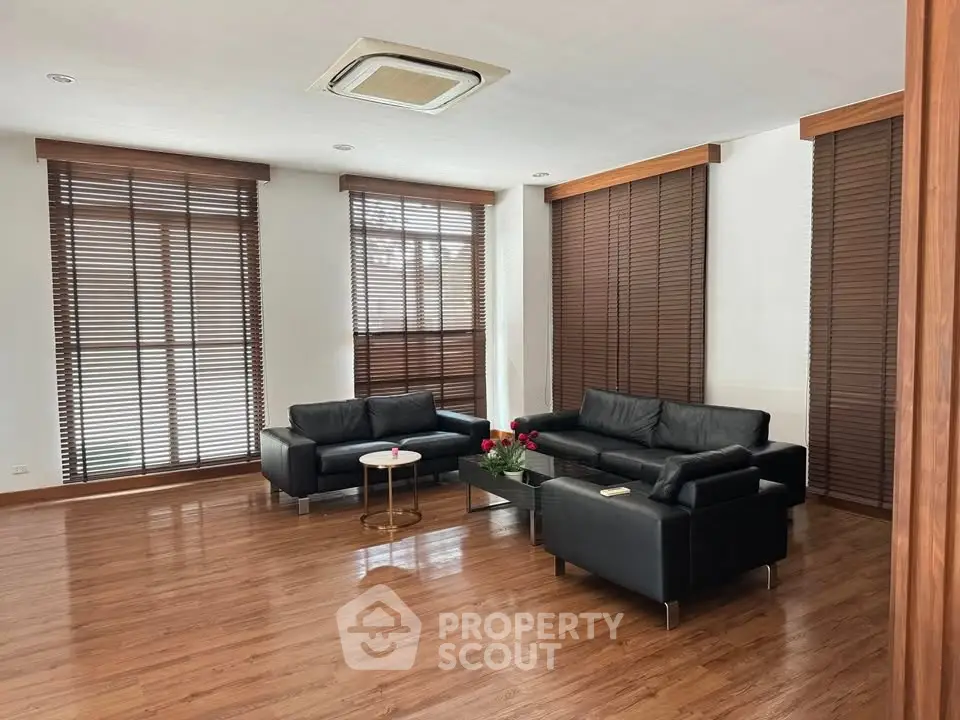 Spacious modern living room with sleek black leather sofas and wooden flooring, perfect for relaxation.