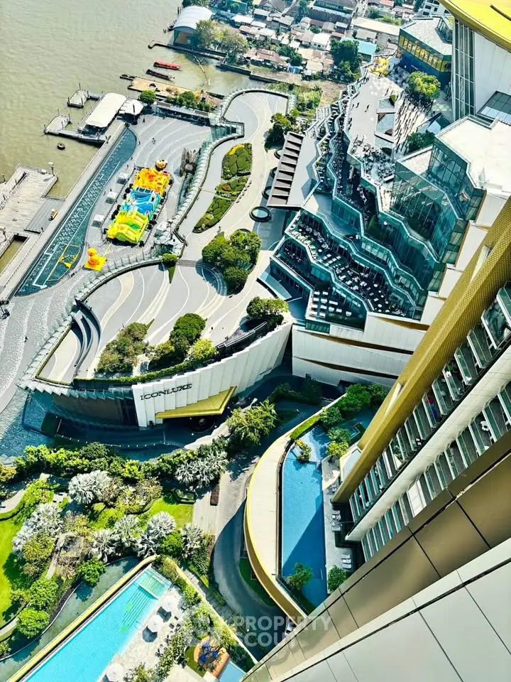 Stunning aerial view of modern riverside building with lush gardens and luxurious pool area.
