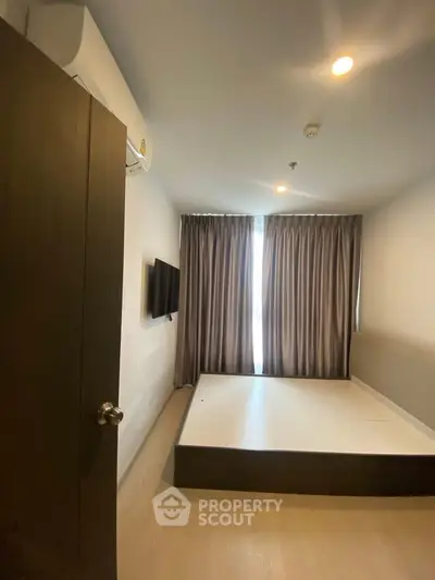 Modern bedroom with minimalist design, featuring a wall-mounted TV and large window with curtains.