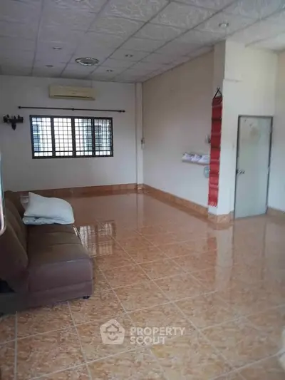 Spacious living room with tiled flooring and brown sofa, featuring large windows for natural light.