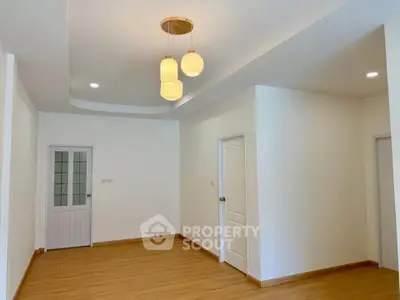 Spacious empty room with elegant ceiling lights and wooden flooring, perfect for customization.