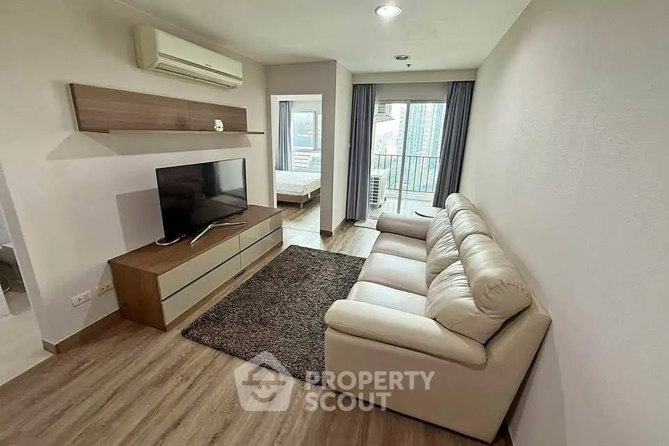 Modern living room with cozy sofa and TV, leading to a balcony with city views.