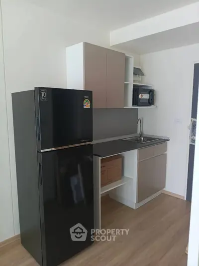 Modern kitchen with sleek black fridge and compact cabinetry in a stylish apartment.