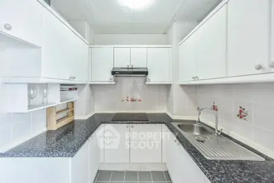 Modern kitchen with sleek white cabinets and black countertops, featuring a built-in stove and stainless steel sink.