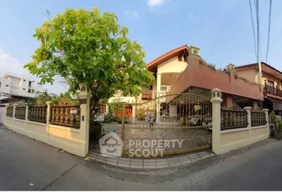 Charming two-story house with ornate gate and lush garden in a serene neighborhood.