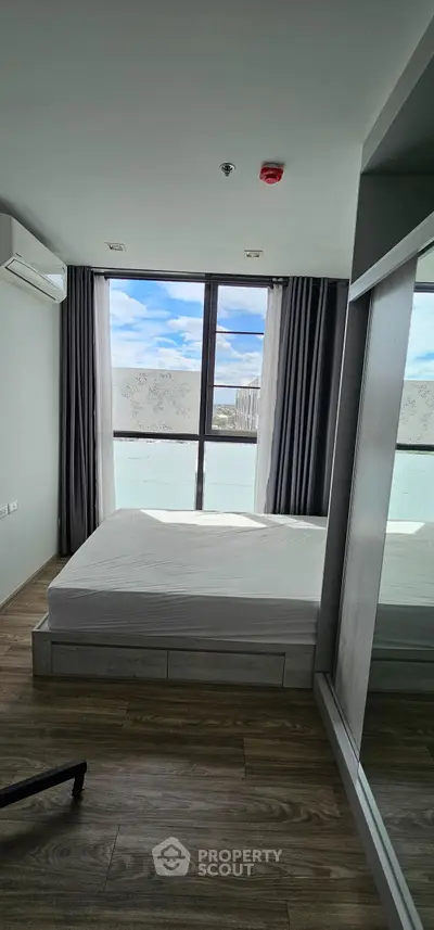 Modern bedroom with large window and wooden flooring, featuring a minimalist design and ample natural light.
