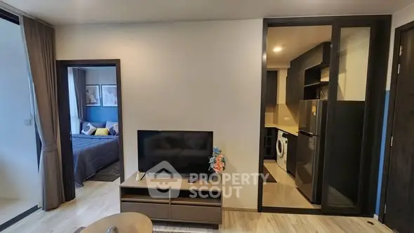 Modern apartment interior with open living room and kitchen, featuring a TV and cozy bedroom view.