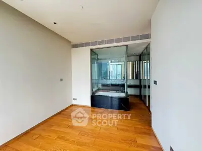 Spacious modern room with wooden flooring and glass-enclosed bathtub, ideal for luxury living.