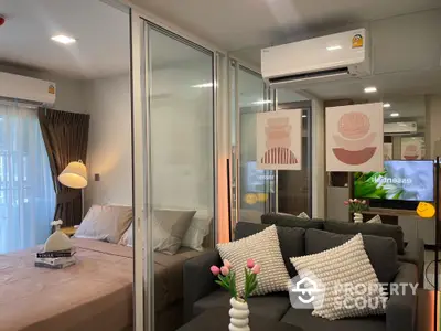 Modern studio apartment with cozy living area and stylish bedroom separated by glass partition.