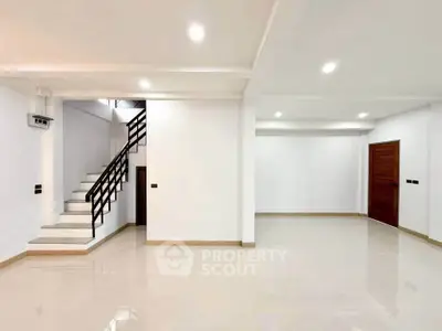 Spacious modern living room with sleek staircase and polished tile flooring in a contemporary home.