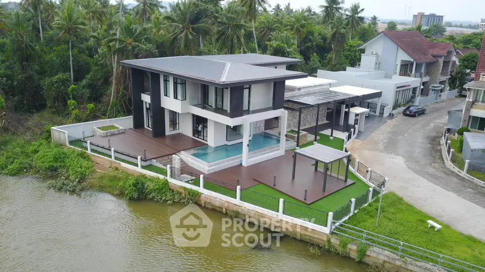 Luxurious modern riverside villa with private pool and spacious deck, surrounded by lush greenery.