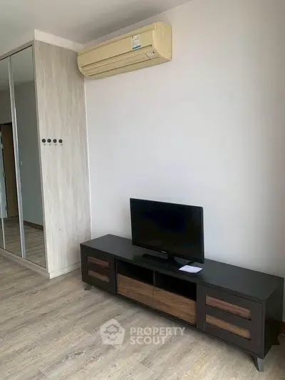 Modern living room with sleek TV stand and mirrored wardrobe, featuring air conditioning and stylish wood flooring.