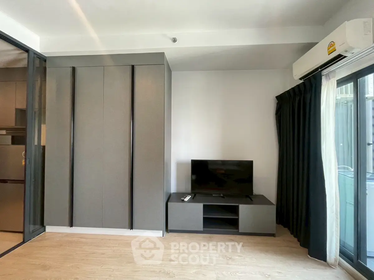 Modern living room with sleek TV stand and large wardrobe, featuring a glass sliding door and air conditioning.