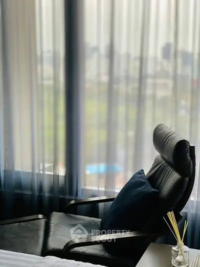 Elegant modern living room with a sleek black leather chair and large windows offering a serene city view.