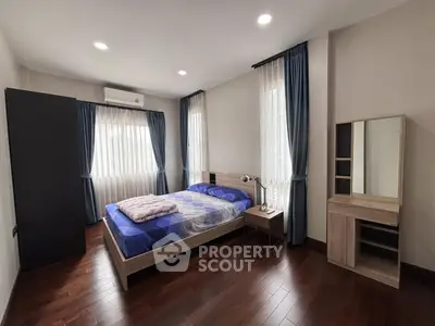 Spacious bedroom with elegant wooden flooring and natural light from large windows.