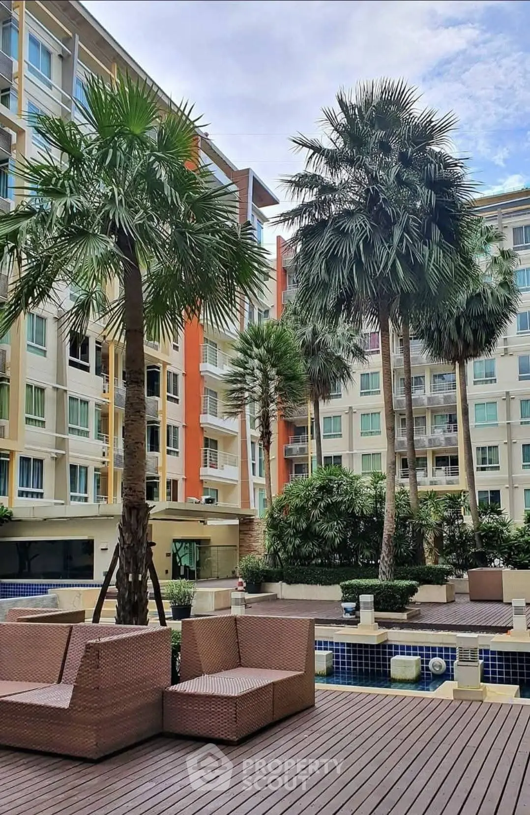 Modern apartment complex with lush garden and poolside seating area.