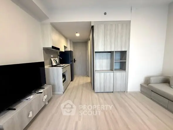 Modern apartment interior with sleek kitchen and cozy living area, featuring light wood finishes and open layout.