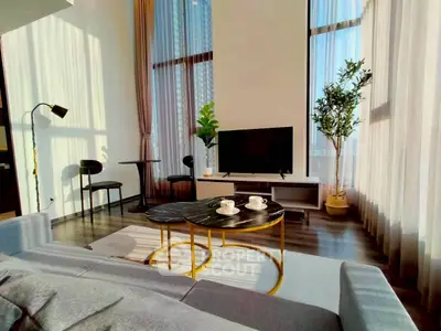 Modern living room with high ceilings, large windows, and stylish furniture in a sunlit apartment.