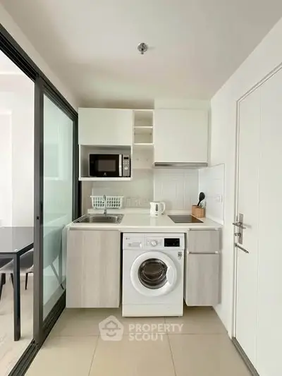 Modern compact kitchen with washing machine and microwave in sleek apartment.