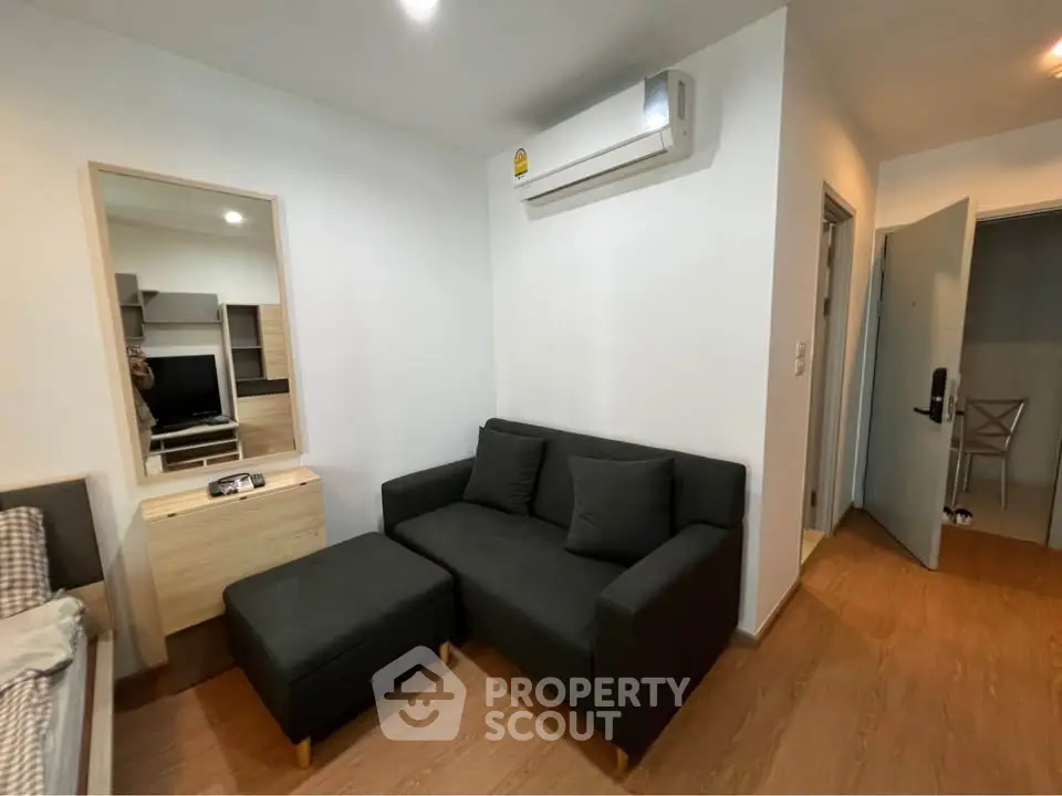 Modern living room with sleek black sofa and wooden flooring, featuring a wall-mounted air conditioner.