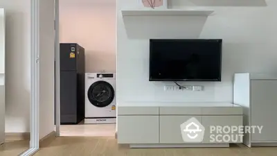 Modern living room with TV and adjacent laundry area featuring washing machine and fridge.