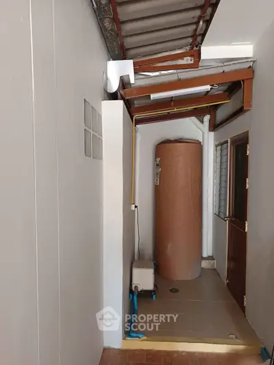 Compact utility area with water tank and tiled flooring in a residential property.