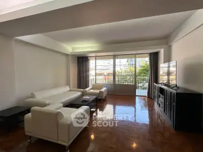 Spacious living room with modern white furniture and large windows offering natural light and city views.
