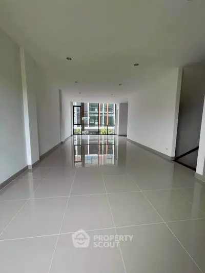 Spacious modern living room with large windows and glossy tiled flooring.