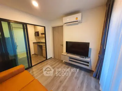 Modern living room with sleek design, featuring a wall-mounted TV, air conditioning, and a view into a compact kitchen.