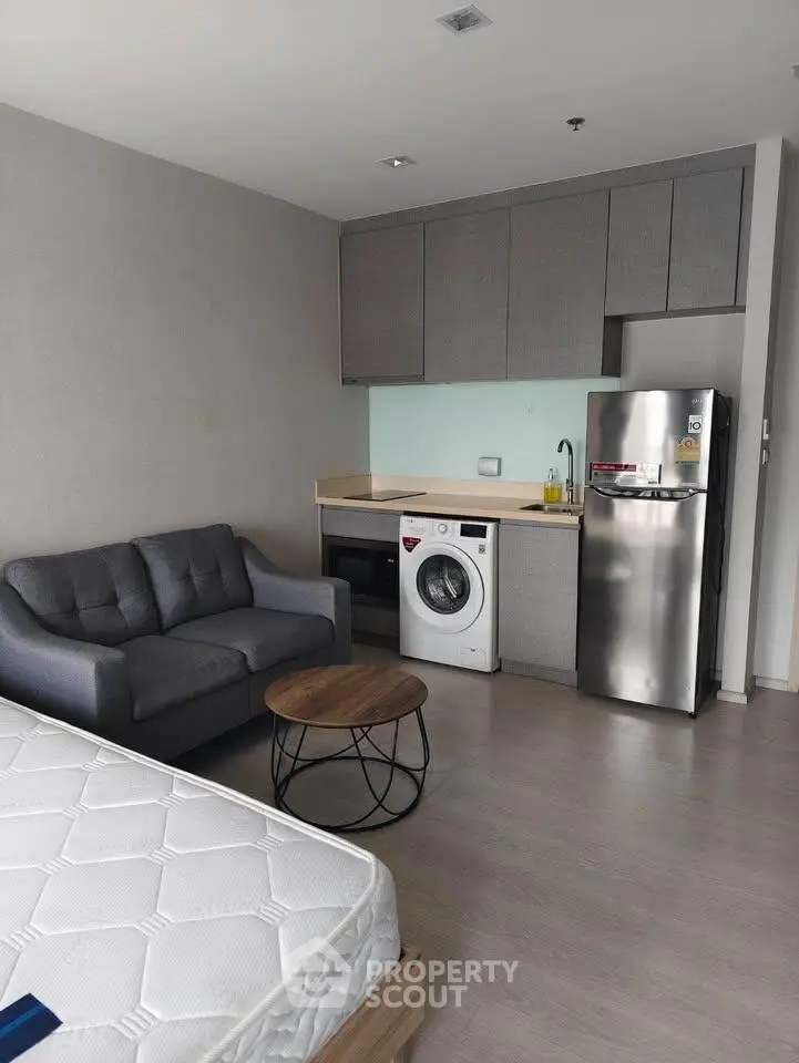 Modern studio apartment with compact kitchen and cozy living area featuring a washing machine and sleek appliances.