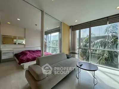 Modern bedroom with large windows and cozy seating area, offering a serene garden view.