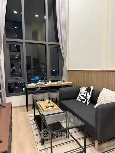 Modern living room with high ceilings and large windows offering city views, featuring stylish furniture and decor.